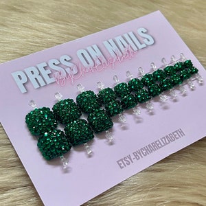 May include: Press-on nails with a green glitter finish. The nails are arranged on a pink card with the text "PRESS ON NAILS By Charrellizabeth" and "ETSY-BYCHARRELIZABETH".