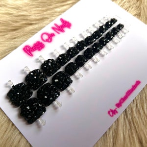 May include: Press-on nails with a black, sparkly finish. The nails are arranged in rows on a white card with the text "Press On Nails" in pink letters and "Art By Charlizebeth" in pink letters.
