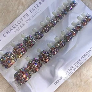 Peut inclure: Un ensemble de 10 ongles press-on avec des paillettes irisées et des strass. Les ongles sont disposés en deux rangées sur une carte blanche avec le texte "BY CHARLOTTE ELIZABETH PRESS ON NAILS" et "THANK YOU FOR YOUR PURCHASE SHOP ETSY - BYCHARELIZABETH".