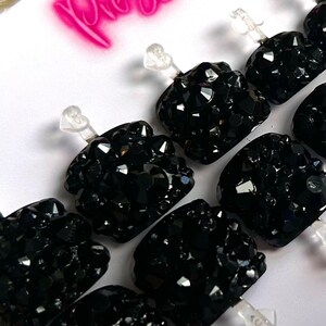 May include: Set of ten black press-on nails with clear adhesive tabs. Each nail is covered in black rhinestones.