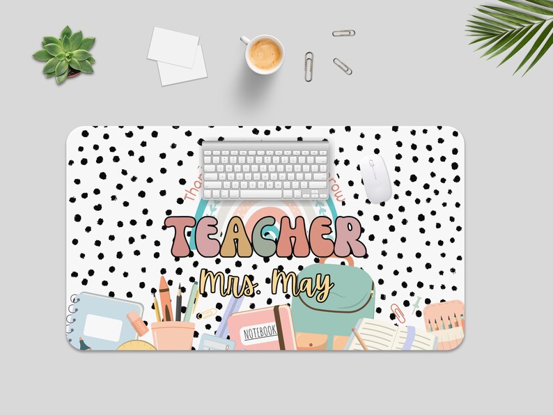 May include: A white desk mat with black polka dots and the text "Teacher Mrs. May". The mat features a rainbow, a backpack, pencils, and other school supplies.