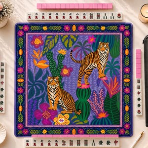 May include: A square mahjong mat featuring a vibrant purple background with two tigers, green cacti, and colorful flowers. The border has a floral pattern. Surrounding the mat are rows of mahjong tiles with Chinese characters, a black carrying case, a small white bowl with two gold rings, and a candle.