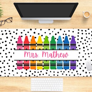 May include: A white desk mat with a black polka dot pattern. The mat features a row of colorful crayons with the text "mrs. mathew" in pink.