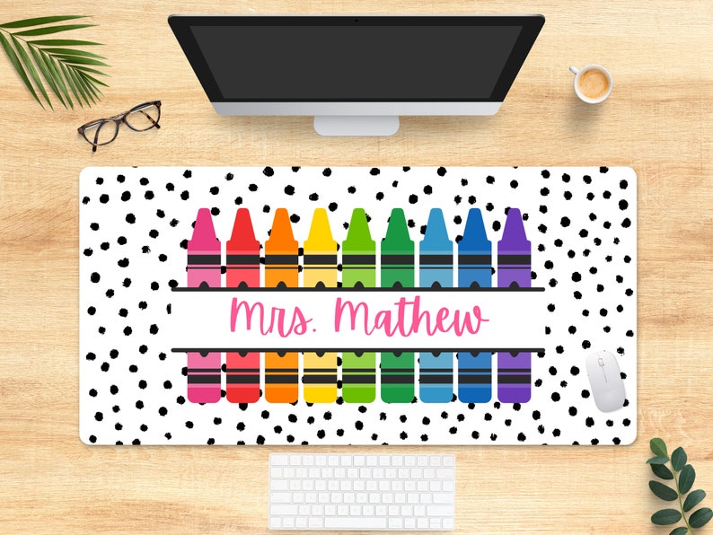 May include: A white desk mat with a black polka dot pattern. The mat features a row of colorful crayons with the text "mrs. mathew" in pink.