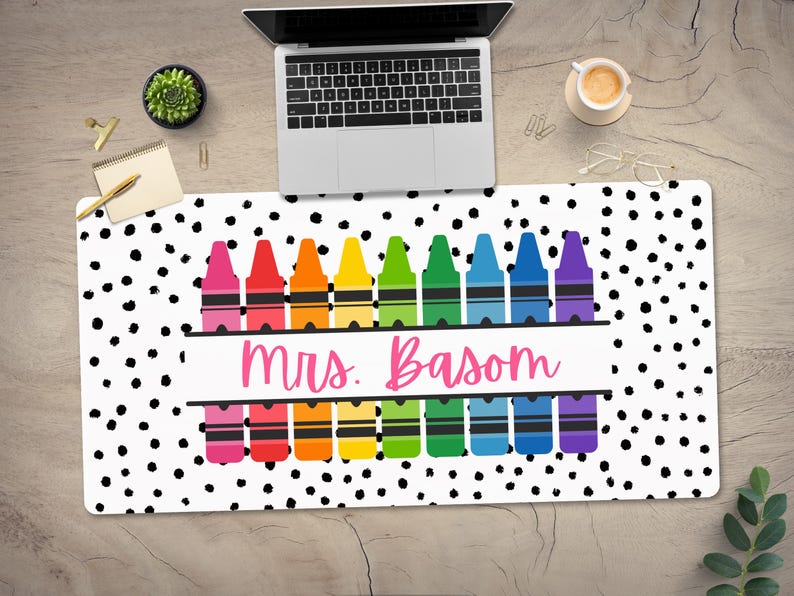 May include: A white desk mat with black polka dots and a row of rainbow colored crayons with the text "mrs. Basom" in pink.