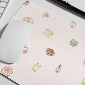 May include: A pink and white mouse pad with a repeating pattern of various desserts and drinks, including cupcakes, cakes, macarons, and boba tea.