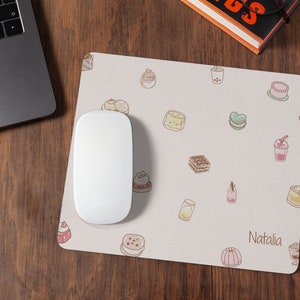 May include: A white mouse pad with a light pink background and a variety of colorful cartoon desserts and drinks. The text "Natalia" is printed in the bottom right corner.