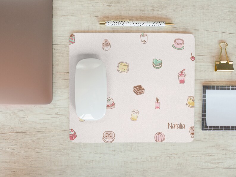 May include: A pink mouse pad with a variety of cute food illustrations, including cakes, pastries, and drinks. The mouse pad has the name "Natalia" printed on it.