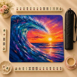 May include: A square play mat featuring a vibrant oil painting of a large ocean wave at sunset with deep blues, purples, and fiery oranges. The mat is surrounded by ivory-coloured Mahjong tiles, a black cylindrical carrying case, and a small teacup.