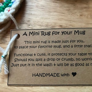 May include: A handmade mini rug with a tag that reads "A Mini Rug for your Mug". The rug is made of colorful yarn and is designed to protect tables from mugs and snacks. The tag also says it's washable.