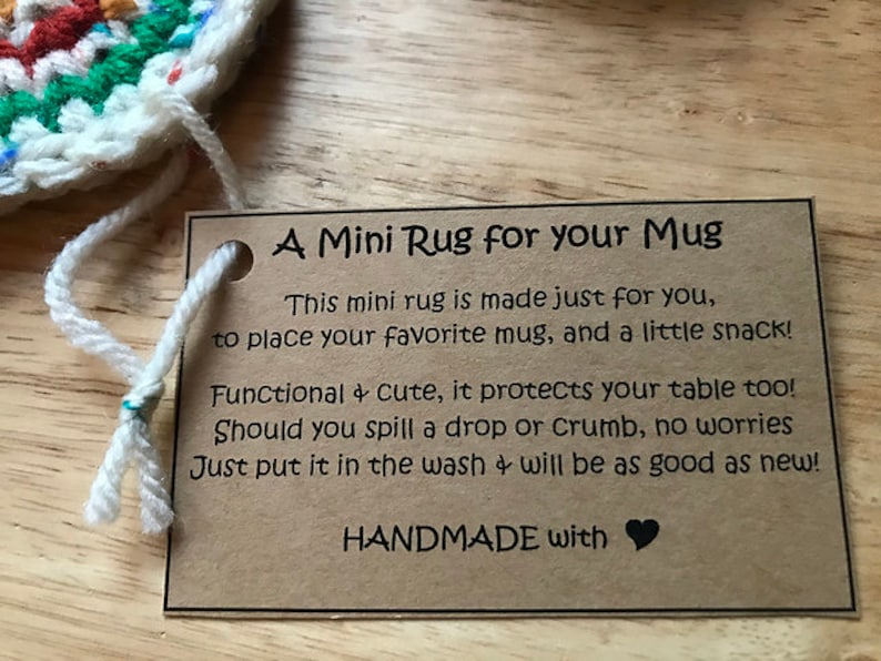 May include: A handmade mini rug with a tag that reads "A Mini Rug for your Mug". The rug is made of colorful yarn and is designed to protect tables from mugs and snacks. The tag also says it's washable.
