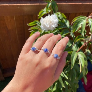 May include: Three silver wire wrapped rings with blue sodalite stones. The rings are on a person's hand.