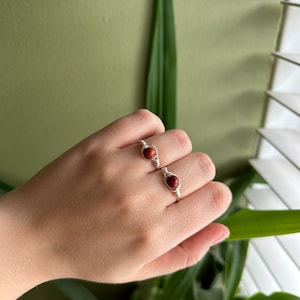 May include: Two silver wire wrapped rings with red gemstone beads. The rings are on a person's finger.