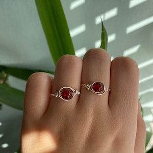 May include: Two silver rings with red gemstone accents. The rings are on a person's finger.