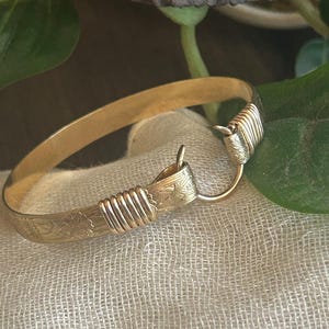 Puede incluir: Un brazalete de oro con un diseño floral y un cierre de alambre.
