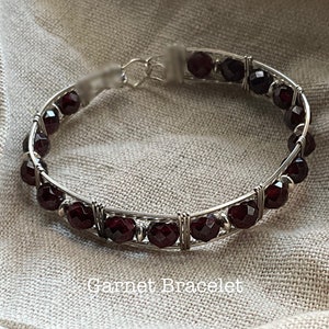 May include: A silver wire wrapped bracelet with red garnet beads. Garnet Bracelet.