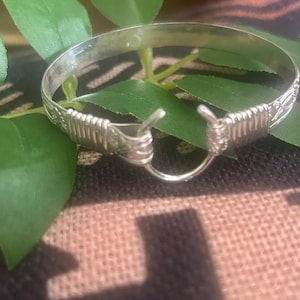 May include: A silver bangle bracelet with a decorative design. The bracelet has a hinged clasp.