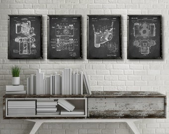 May include: Four black and white framed prints of vintage camera patent drawings. The prints are hanging on a white brick wall above a wooden shelf with books stacked on it.