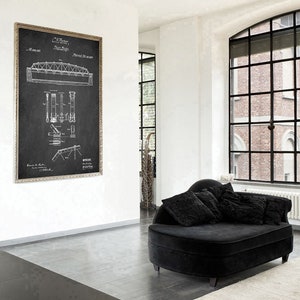 May include: A black and white vintage patent drawing of a bridge design. The drawing is framed in a silver frame and hanging on a white wall. A black chaise lounge with black pillows is in the foreground.