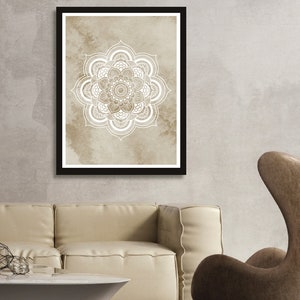 May include: A framed print of a white mandala design on a beige background. The mandala is intricate and detailed, with a circular pattern of flowers and leaves.