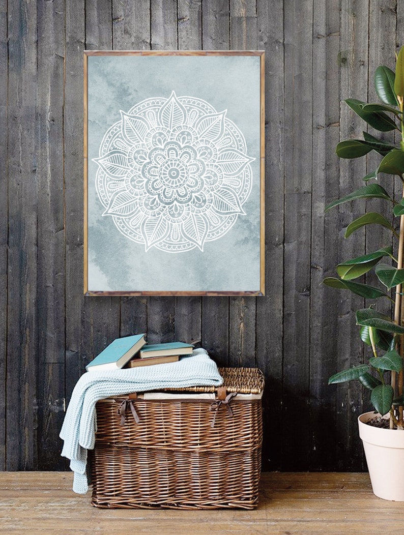 May include: A framed print of a white mandala design on a blue watercolor background. The mandala is intricate and detailed, with a floral pattern. The print is hanging on a dark gray wood wall.