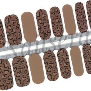 May include: Nail wraps in shades of brown and tan. Some wraps display a brown leopard print with black heart shapes, while others are plain tan. The wraps are presented on a silver backing.