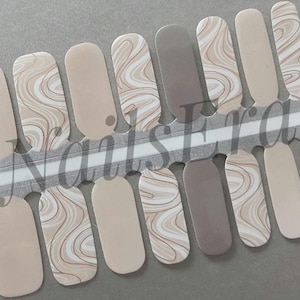 May include: Nail wraps in a neutral colour palette. The wraps feature a mix of solid beige and swirling marble designs in beige, white, and taupe. The wraps are on a grey backing with the word "NailsEra" printed on it.