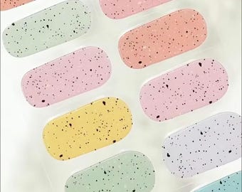 May include: A sheet of pastel-colored nail stickers with a speckled design. The colors include light blue, light green, light pink, yellow, and lavender.