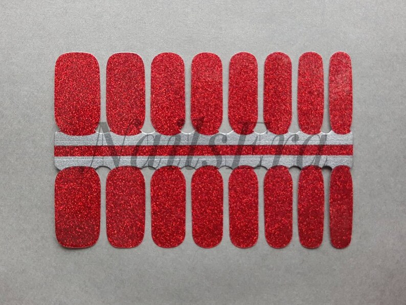 Puede incluir: Una hoja de envolturas de u&ntilde;as de purpurina roja. Las envolturas est&aacute;n dispuestas en dos filas de diez, con una franja plateada y blanca entre las filas.