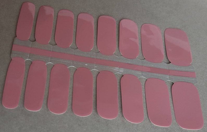 May include: A sheet of mauve-colored nail polish strips. The strips are rectangular with rounded edges, designed to fit various nail sizes. They are arranged on a silver backing with a pinkish-mauve strip.