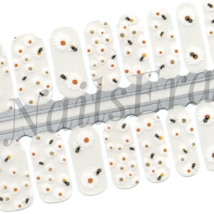 May include: White nail polish wraps with a pattern of white daisies and small yellow bees. The wraps are arranged on a silver and white backing.