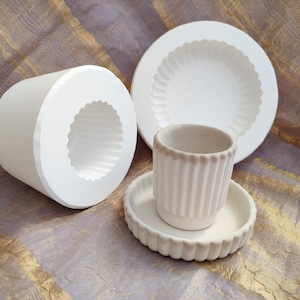 May include: Three white ceramic molds for making planters. The molds are in different sizes and shapes. The largest mold is a round dish with a scalloped edge. The medium mold is a cylinder with a scalloped top. The smallest mold is a small cup with a scalloped edge.
