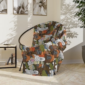 Pode incluir: Uma manta estampada sobre uma cadeira preta. A manta apresenta um design repetido de personagens de desenhos animados em várias cores, incluindo marrom, verde e branco. A cadeira tem uma estrutura de metal preta e um encosto tecido.