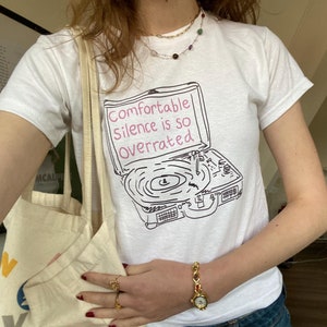 May include: White t-shirt with a black and white illustration of a record player and the text "Comfortable silence is so overrated".