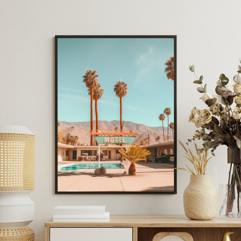 Op de afbeelding: Een ingelijste kunstdruk met een woestijnmotelsc&egrave;ne met een zwembad, palmbomen en bergen onder een heldere lucht. Het bord boven het zwembad toont duidelijk het woord MOTEL in witte hoofdletters tegen een blauwgroene achtergrond.