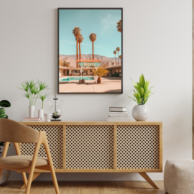 Op de afbeelding: Een ingelijste wandkunstprint met een woestijnmotelsc&egrave;ne met een zwembad, palmbomen en bergen op de achtergrond. Het bord boven het zwembadgedeelte toont duidelijk het woord MOTEL in dikke, donkere letters tegen een lichte achtergrond.
