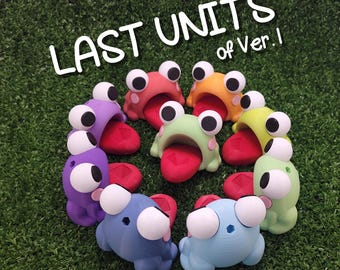 May include: A group of eight colorful frog-shaped figurines with large eyes and open mouths. The figurines are arranged in a circle on a green surface. The text "LAST UNITS of Ver.1" is displayed above the figurines.