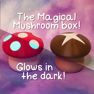 Puede incluir: Dos cajas con forma de hongo que brillan en la oscuridad. Una es roja con puntos blancos y azules, la otra es marrón con una estrella blanca. El texto "The Magical Mushroom box! Glows in the dark!" está escrito debajo de los hongos.