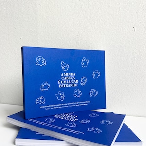 Puede incluir: Una pila de libros azules con ilustraciones blancas de caras y el texto "A MINHA CABEÇA É UM LUGAR ESTRANHO". Los libros están apilados uno encima del otro.