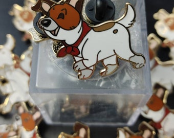 May include: A close-up of a white and brown enamel pin featuring a cartoon dog wearing a red bandana. The pin has a gold finish and a black pin back.