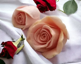May include: Two pink roses carved from fruit, one with a single layer of petals and the other with multiple layers, are displayed on a white fabric background. A red rose with a green stem and leaf is also visible.