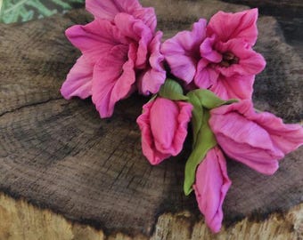 May include: Close-up of vibrant pink flowers with green stems and buds, arranged on a rustic wooden surface. The flowers have multiple petals and are in full bloom, with a fern in the background.