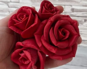 May include: Four red roses, each with a different size and shape, are held in a hand. The roses are made of a soft, velvety material.