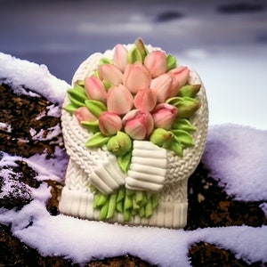 Puede incluir: Un suéter de punto blanco con un ramo de tulipanes rosas sostenido en las mangas. El suéter está sobre una superficie nevada.