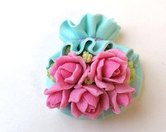 May include: A light blue fabric pouch with a ruffled edge, decorated with a cluster of pink roses and green leaves.