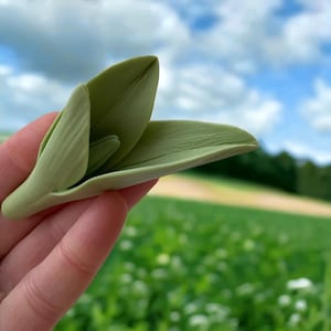 May include: A light green, hand-crafted flower made of polymer clay. The flower is open and has a delicate, realistic appearance.