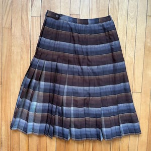 May include: A brown and blue plaid pleated skirt. The skirt features a button fastening at the waist and falls to the mid-thigh. The fabric has a slight sheen, and the pleats create a flowing shape. The skirt is approximately 60 cm in length.