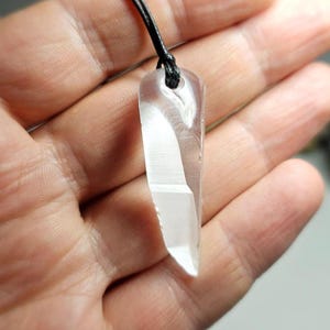 Può includere: Un ciondolo di cristallo trasparente a forma di punta lunga e sottile, appeso a un cordoncino nero.