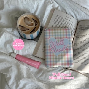 Könnte beinhalten: Eine transparente Kindle-Hülle mit pastellfarbenem Karomuster und einem hellblauen Herz-Motiv mit dem Text Well Read. Die Hülle liegt auf einem offenen Buch neben einem Eiskaffee und einer rosa Summer Fridays Lippenbalsamtube. Ein rosa Digital-Download-Symbol.