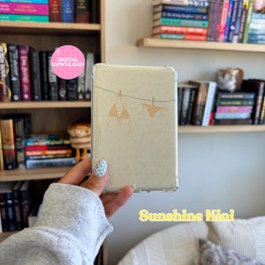 Puede incluir: Una funda protectora transparente para lector electrónico con fondo color crema, un patrón sutil de puntos pequeños y un dibujo lineal de un bikini en un tendedero. El texto Sunshine Kini está impreso en amarillo en la parte inferior derecha.